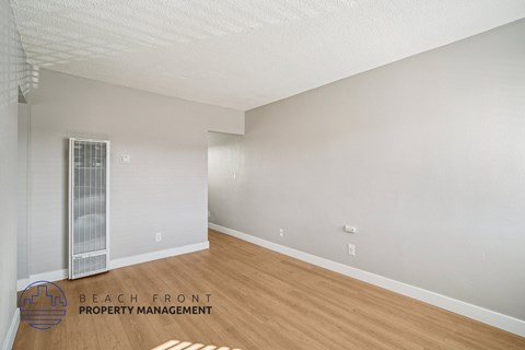 A spacious room with a wooden floor and a window with blinds.