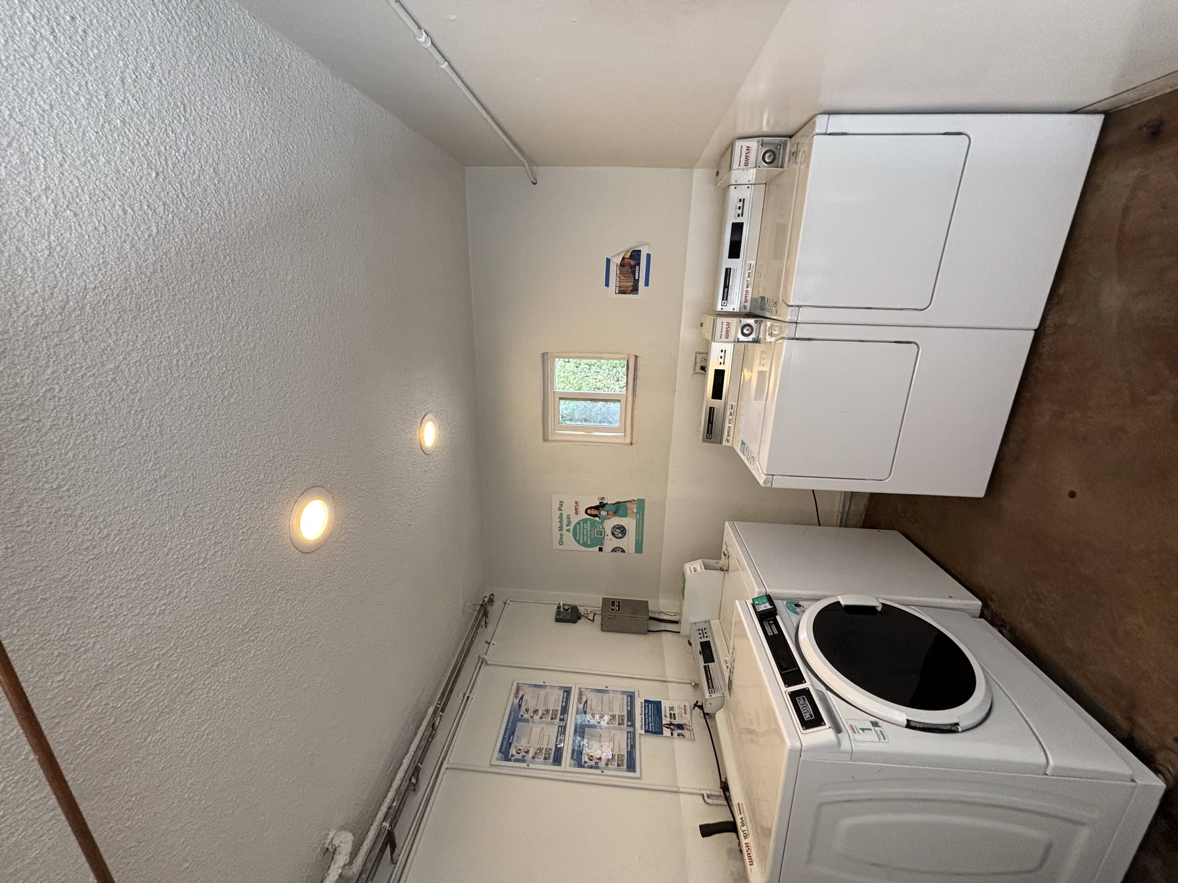 A small white washing machine is in a small room with a window.