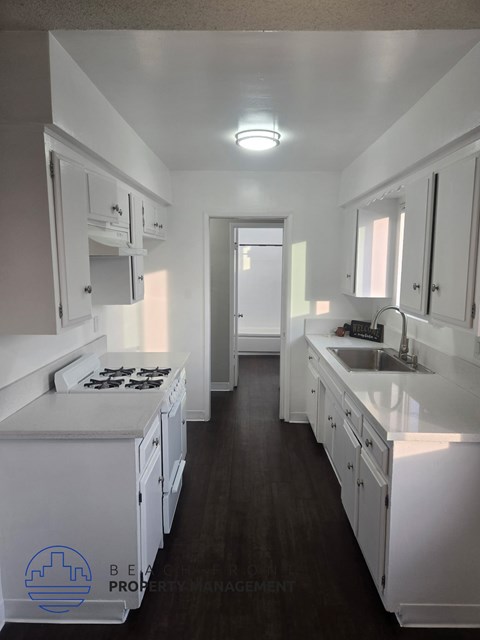 A clean, white kitchen with dark wood floors and a logo for Bel-Air Property Management in the bottom left corner.
