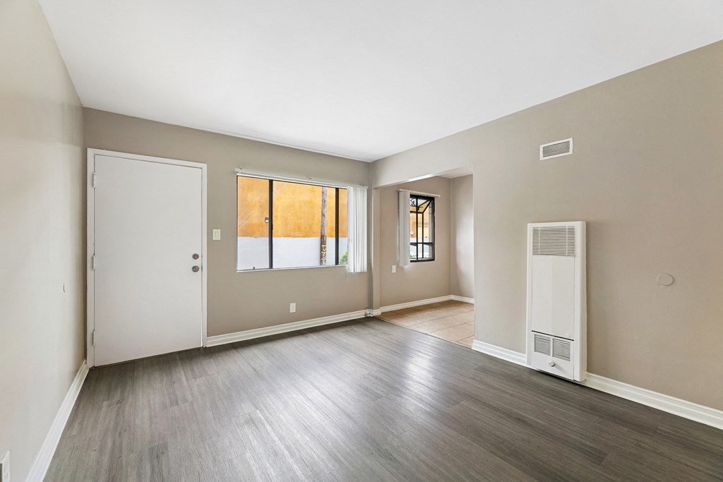 the living room and dining room of an apartment with wood flooring and a window