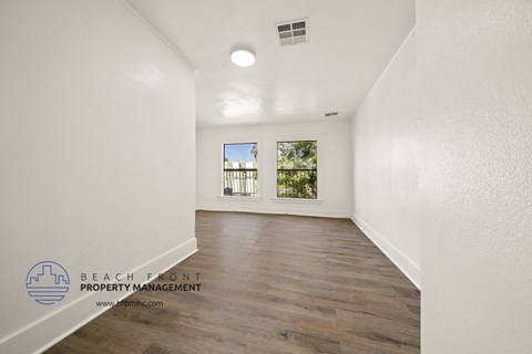 A spacious room with wooden flooring and a window overlooking a green area.