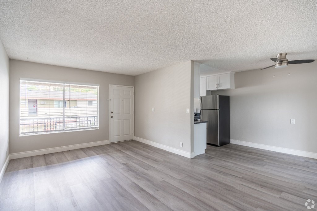 an empty living room with a large window and a kitchen