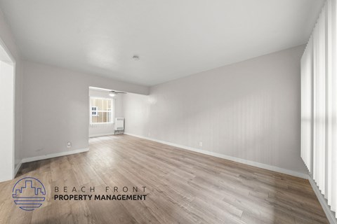 A spacious room with wooden flooring and white walls, managed by Beach Front Property Management.