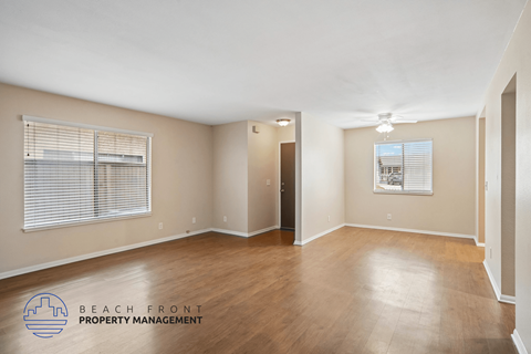 A spacious room with wooden flooring and a logo for Beach Front Property Management.