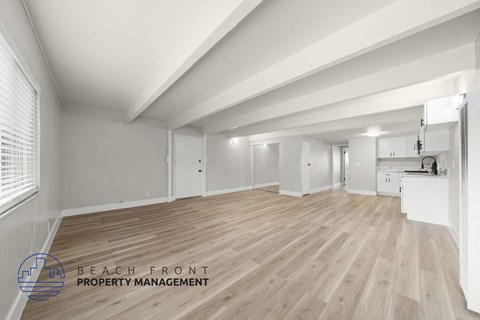 A spacious room with wooden flooring and white walls, with a logo for Beach Front Property Management in the bottom left corner.