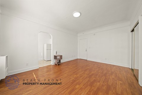 A room with wooden floors and white walls, with a logo for Beach Front Property Management in the bottom left corner.