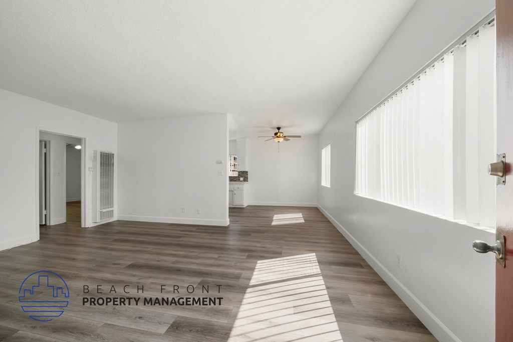 A spacious room with wooden flooring and white walls, with a logo for Beach Front Property Management in the bottom left corner.