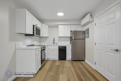 A kitchen with white cabinets and appliances, a wooden floor, and a door on the right.