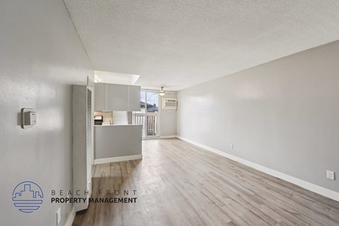 A spacious room with wooden flooring and a logo for Beach Front Property Management in the corner.