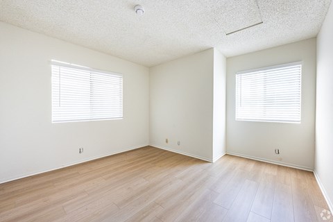 A room with wooden floors and two windows with blinds.
