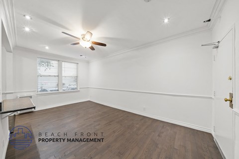 a living room with white walls and wooden floors and a ceiling fan