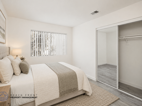 A bedroom with a bed, a window with blinds, a rug, and a mirror.