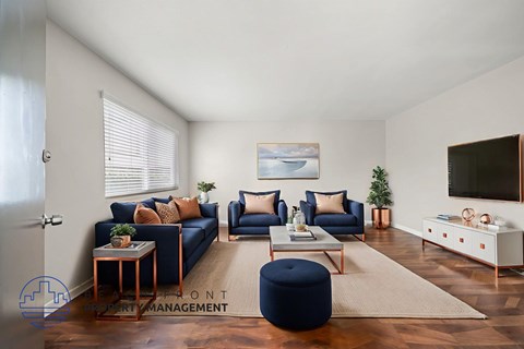 A living room with a blue ottoman and a television on the wall.