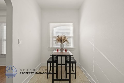 A dining table with two chairs is in a white room with a window.