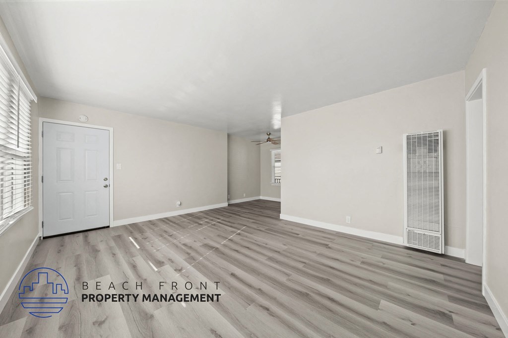 A spacious room with wooden flooring and a logo for Beach Front Property Management.
