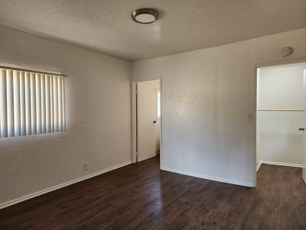 the living room of an apartment with wood flooring and a door to a closet