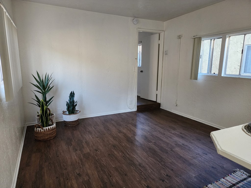 an empty living room with white walls and wooden floors and a potted plant