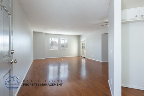 A spacious room with wooden floors and white walls, with a door on the left and a window on the right.