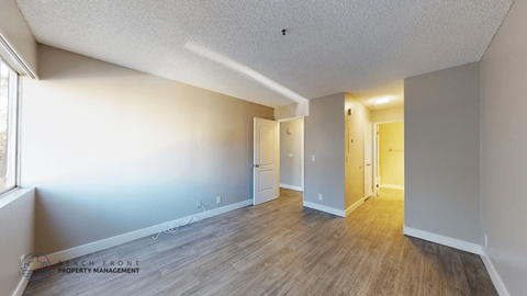 A spacious room with wooden flooring and white walls.
