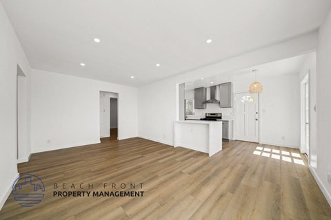 A spacious room with wooden floors and white walls, with a logo for Beach Front Property Management in the bottom left corner.