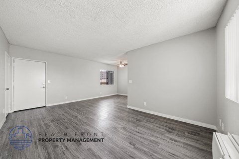 A spacious room with wooden flooring and a logo for Beach Front Property Management in the corner.