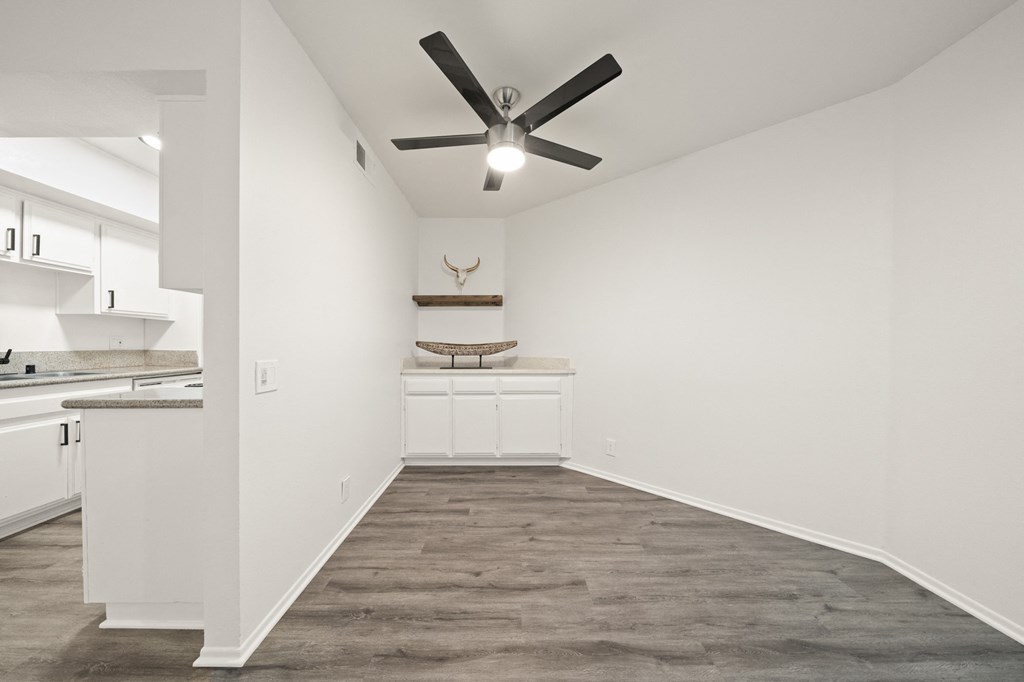 an empty living room with a ceiling fan and a kitchen