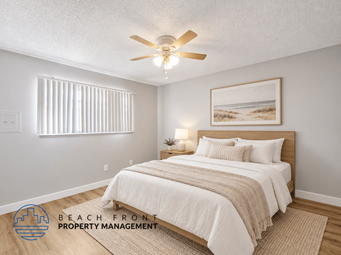 A bedroom with a bed, a ceiling fan, and a painting of a beach scene.