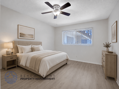 A well-lit bedroom with a large bed, a ceiling fan, and a nightstand with a lamp.