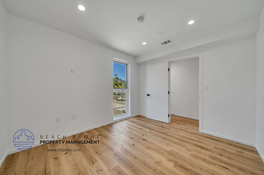 a bedroom with white walls and wood flooring and a door to a hallway