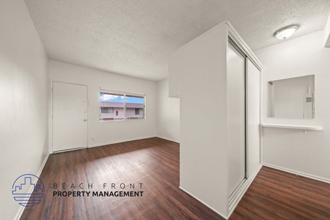 A room with wooden floors and white walls, with a window showing a view of a building outside.