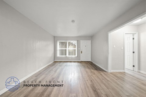 A spacious room with wooden flooring and white walls, with a logo for Beach Front Property Management in the bottom left corner.