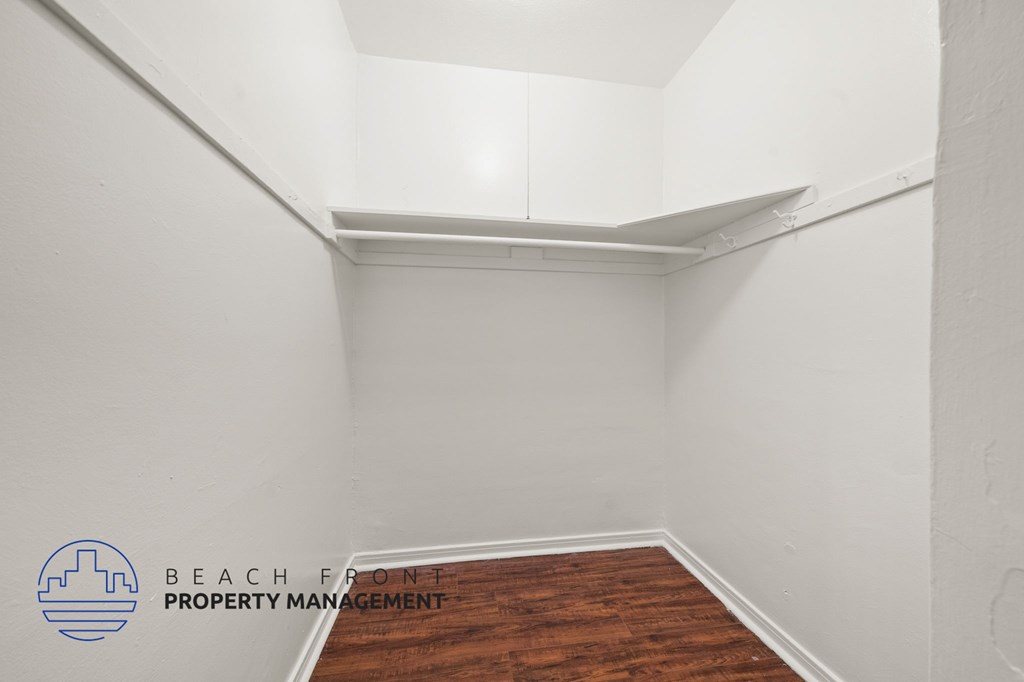 A room with a wooden floor and white walls, with a logo for Beach Front Property Management in the bottom left corner.