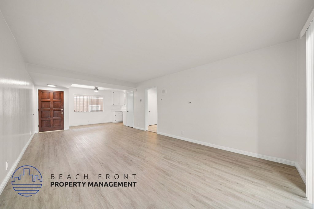A spacious room with wooden flooring and white walls, featuring a door and a window with blinds.