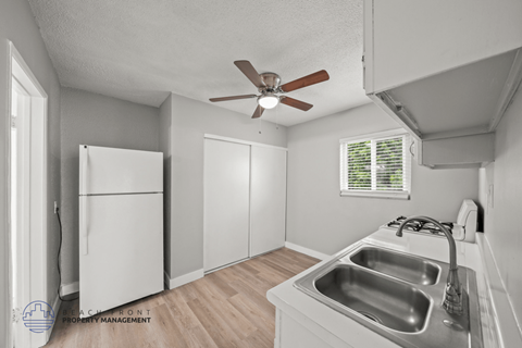 A kitchen with a white fridge, sink and a ceiling fan.