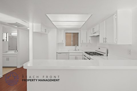 A kitchen with white cabinets and appliances, with a logo for Beach Front Property Management in the bottom left corner.