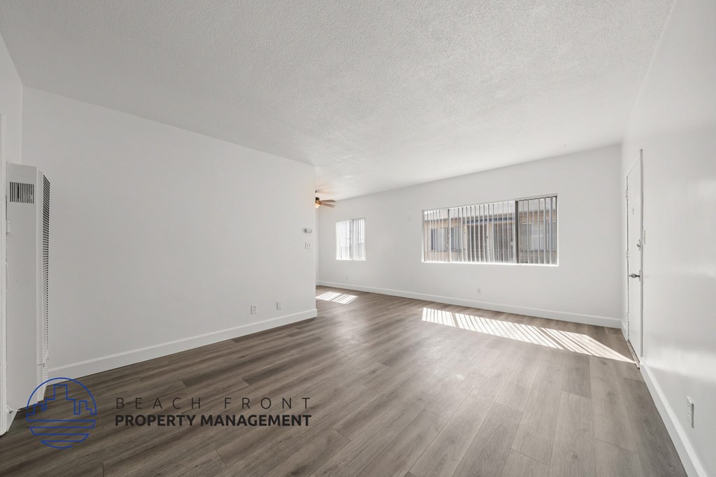 A spacious empty room with wooden flooring and white walls.