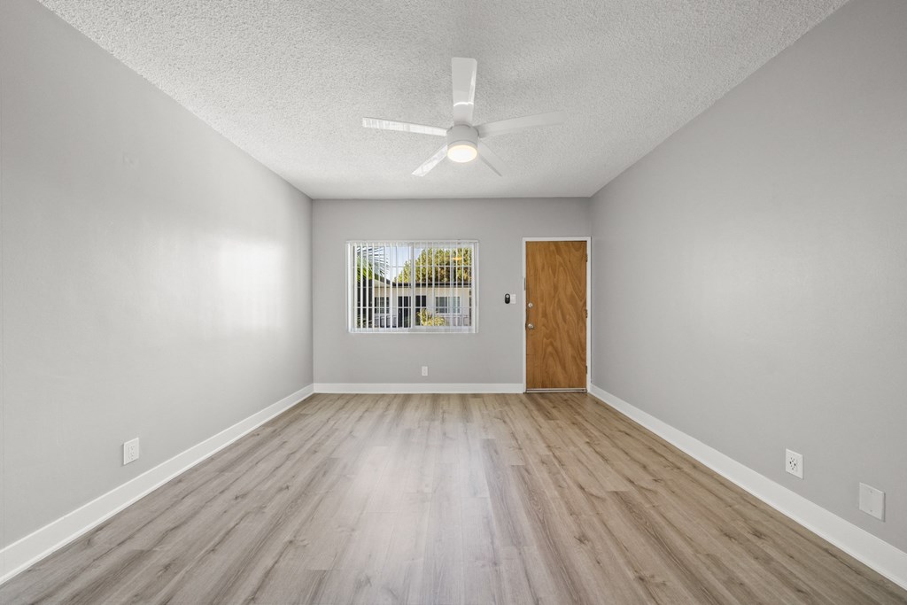 the spacious living room with wood flooring and a ceiling fan