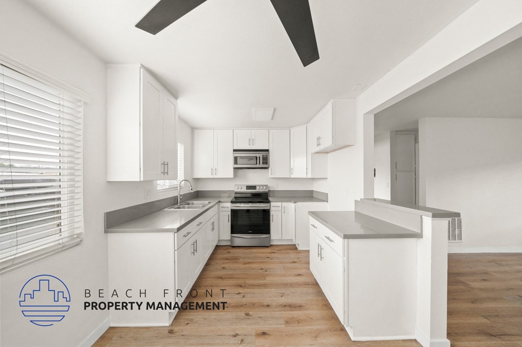 A modern kitchen with white cabinets and a wooden floor.