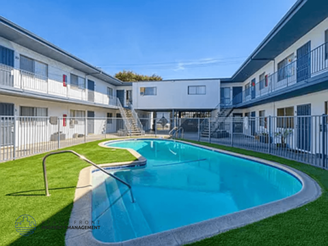 A swimming pool in front of a white building with a metal fence around it.