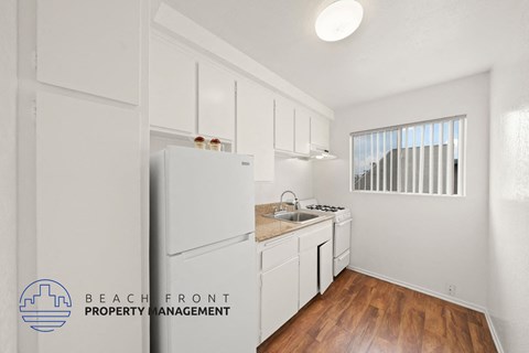 A kitchen with white cabinets and a refrigerator with a logo of Beachfront Property Management.