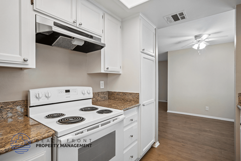 A kitchen with a white stove top oven and white cabinets.