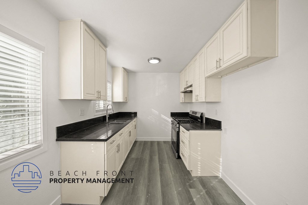 A kitchen with white cabinets and black countertops.
