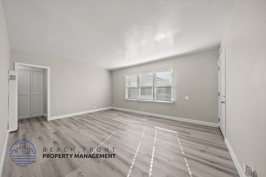 A spacious room with wooden flooring and a window with blinds.