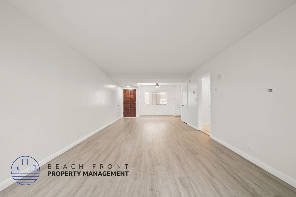 A spacious room with wooden flooring and white walls, with a logo for Beach Front Property Management in the bottom left corner.