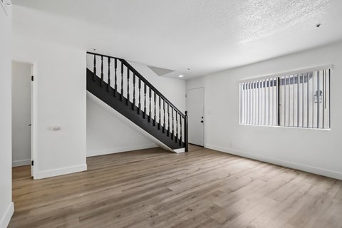 A spacious room with a wooden floor and a staircase.
