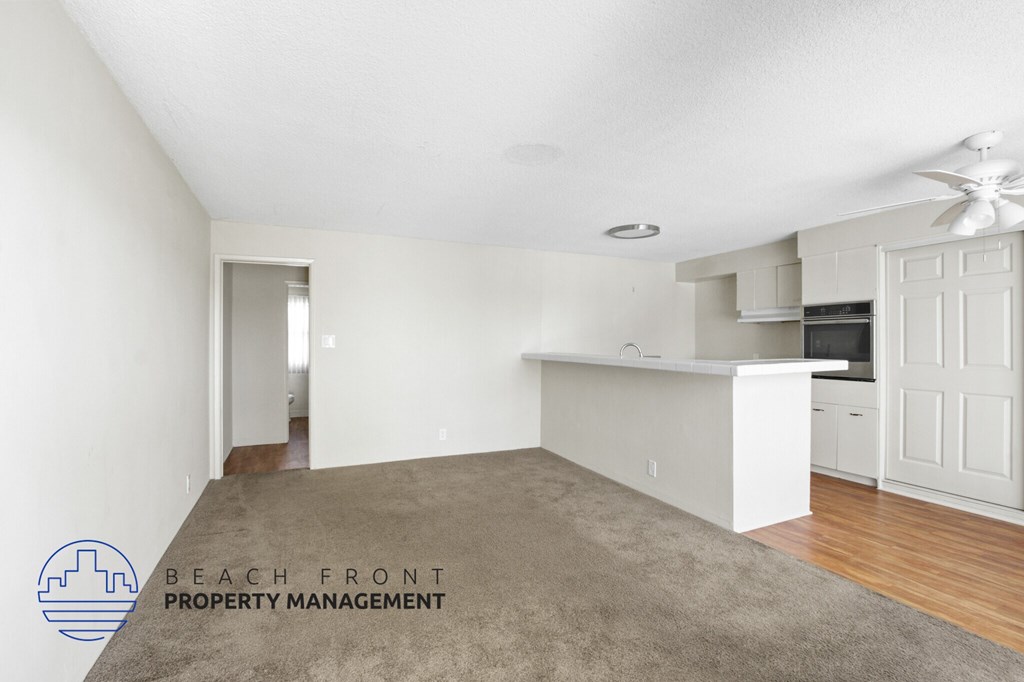 A spacious room with a carpeted floor and a logo for Beach Front Property Management in the corner.