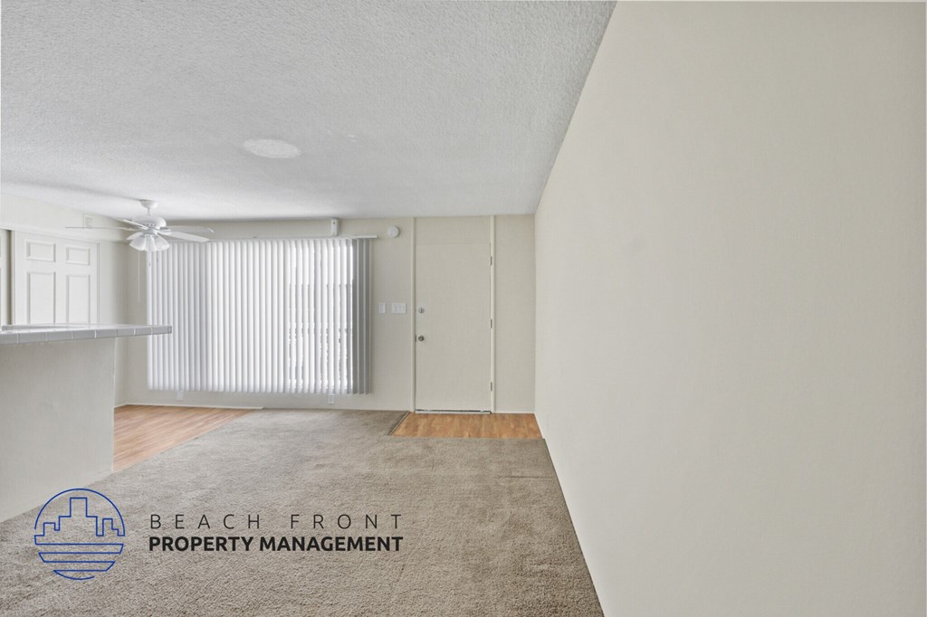 A room with a carpet on the floor and a logo for Beach Front Property Management in the corner.