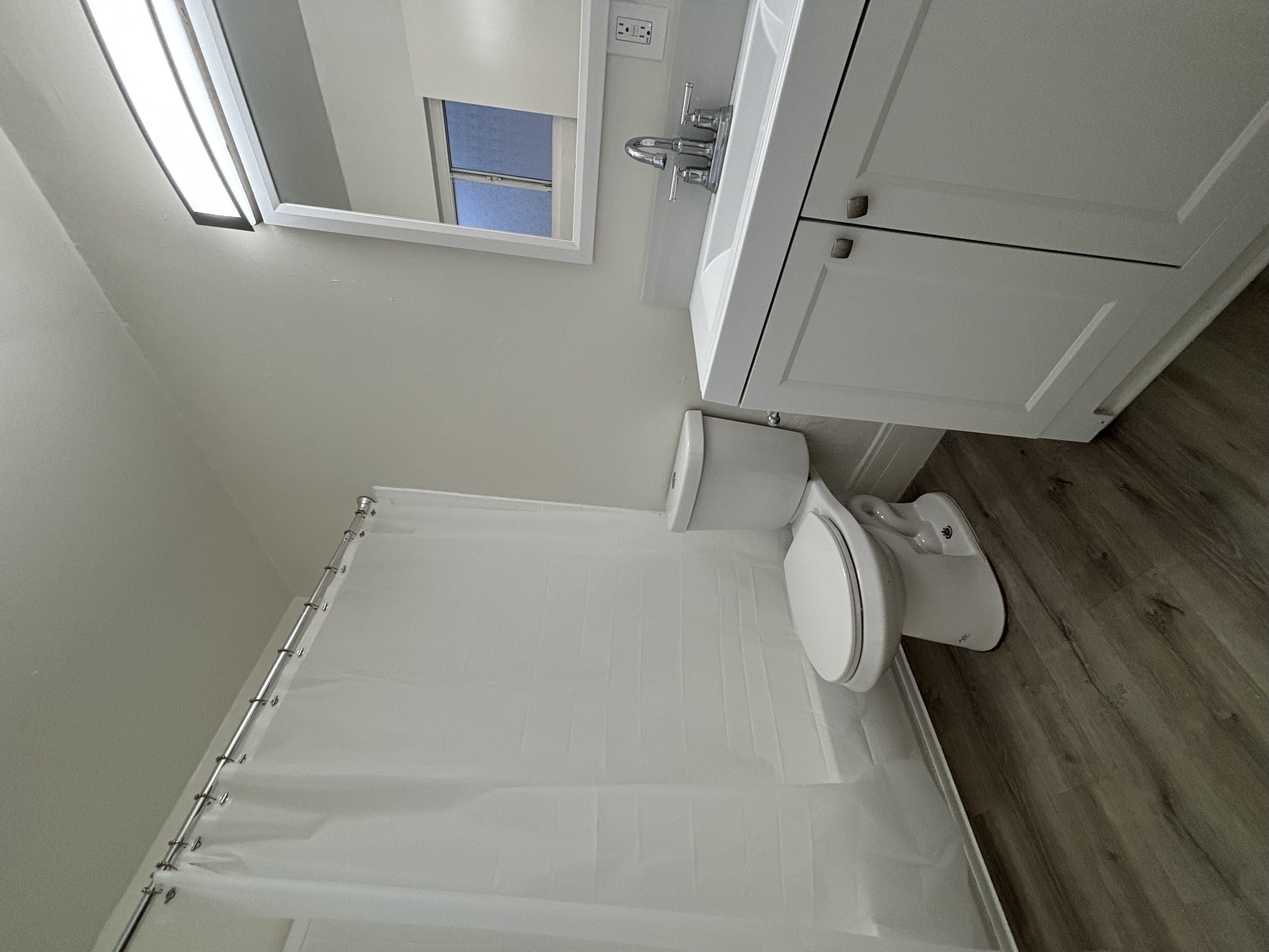 A white toilet with a white tank and a white shower curtain.