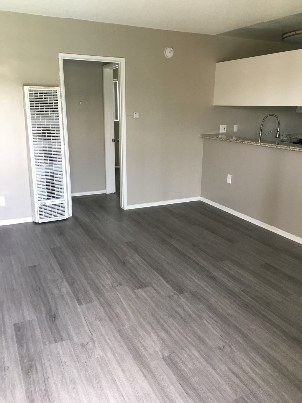 an empty living room with wood floors and a kitchen