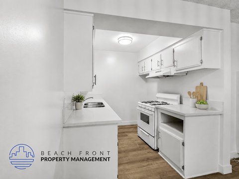 A kitchen with white cabinets and appliances, with the logo of Beach Front Property Management in the bottom left corner.